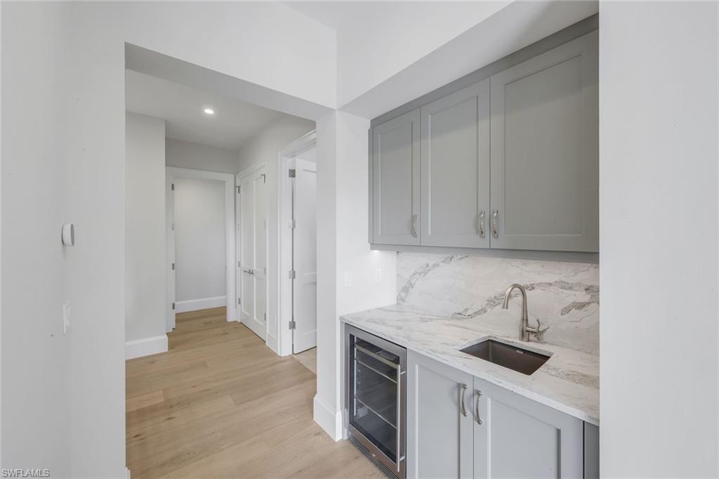 16728 Enclave Circle Naples, FL 34110 - Photo 40 of 49 Indoor wet bar featuring gray cabinets, light stone counters, beverage cooler, light wood-style floors, and recessed lighting