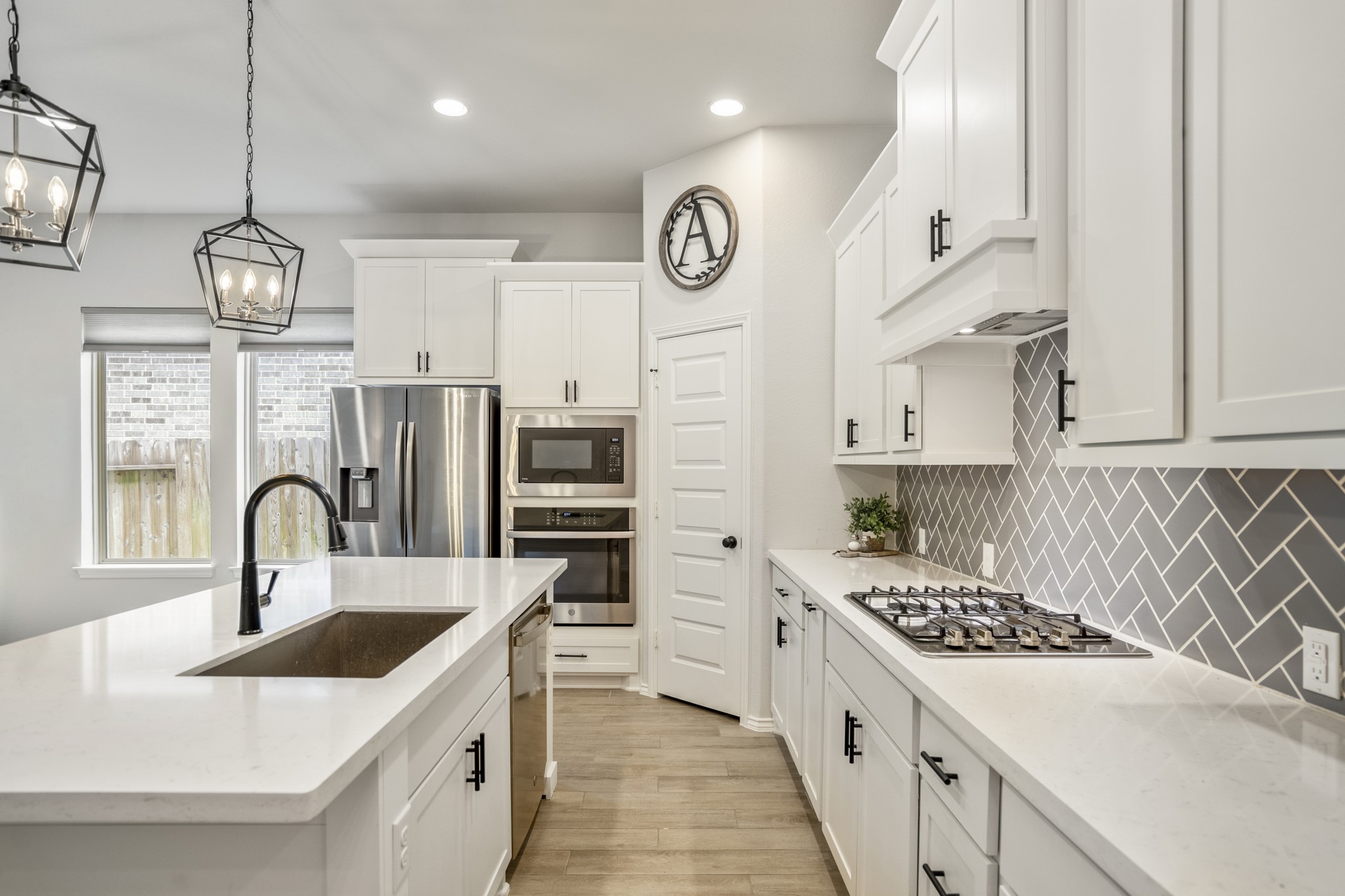 334 Topper Pines Drive Montgomery, TX 77316 - Photo 6 of 49 Welcome to the modern and sleek kitchen featuring a bright white aesthetic with white quartz countertops and cabinets. The black cabinet hardware adds a striking contrast, complemented by the grey tile backsplash in a herringbone pattern, creating a stylish and contemporary look.