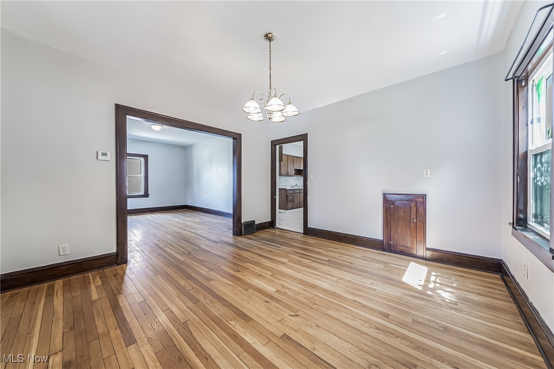 Empty room with light wood-type flooring and an inviting chandelier