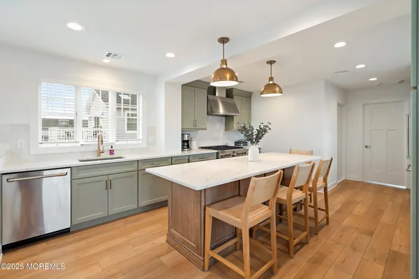 a kitchen with stainless steel appliances a stove a sink dishwasher a dining table and chairs with wooden floor