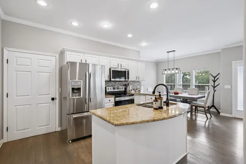 a kitchen with granite countertop a refrigerator a stove a sink a dining table and chairs with wooden floor