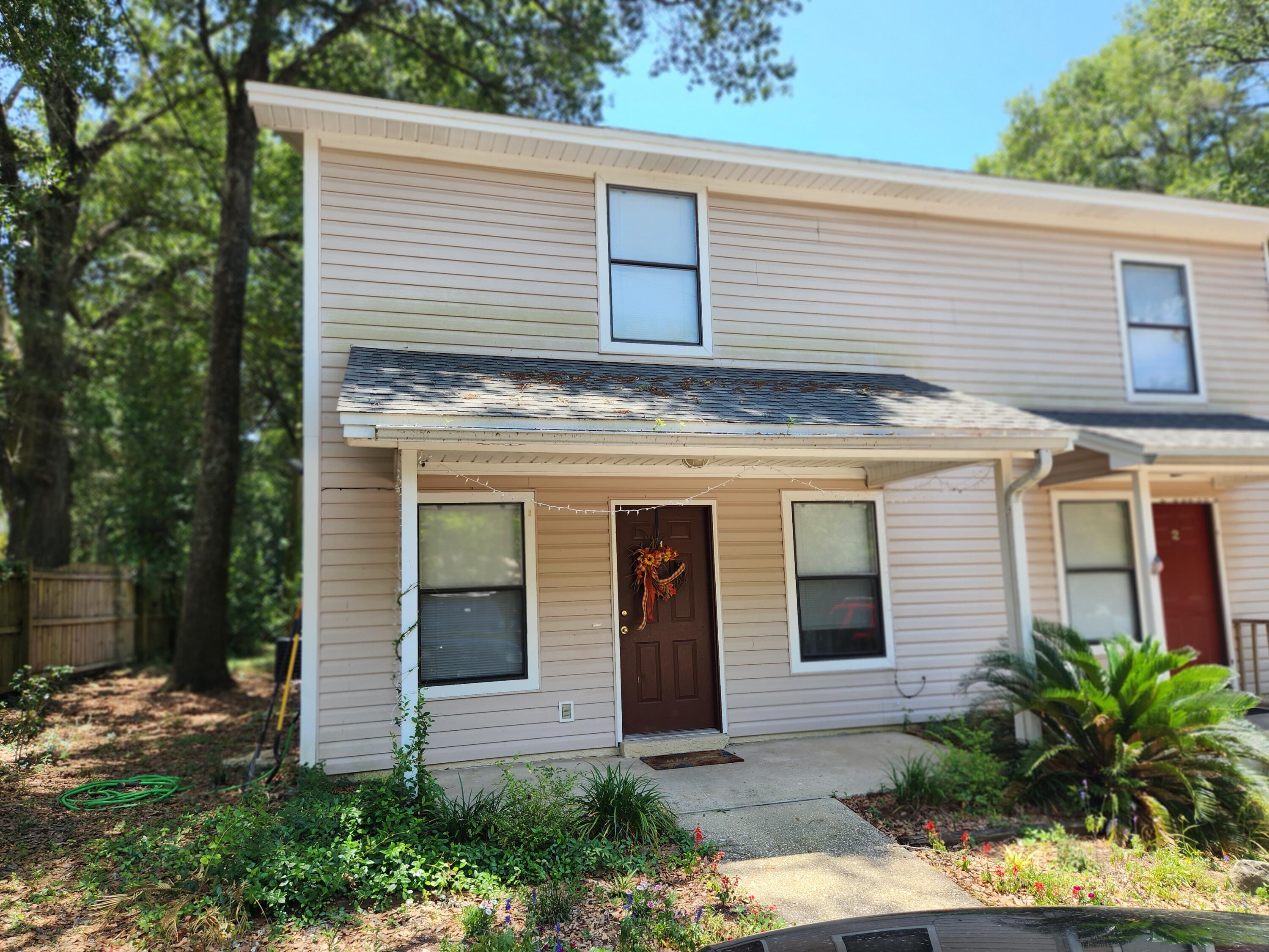 205 Marquette Avenue, Unit 1 Niceville, FL 32578 - Photo 1 of 16 a view of a house with potted plants and a large tree