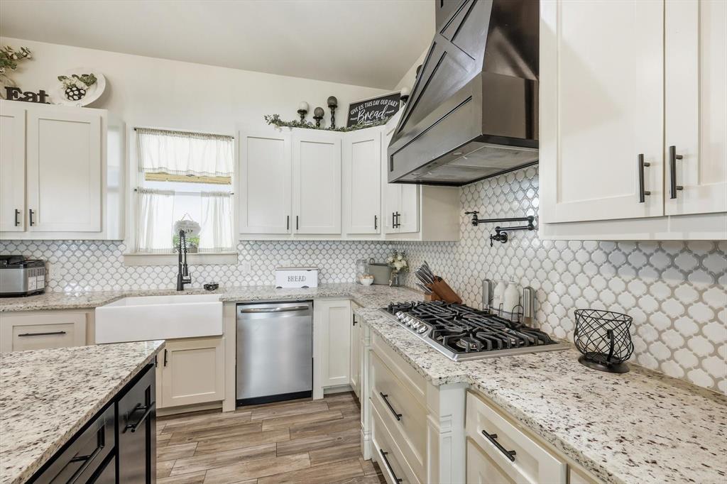 6020 Honeysuckle Road Midlothian, TX 76065 - Photo 12 of 39 Kitchen featuring white shaker-style cabinetry, patterned tile backsplash, light-toned stone countertops, a farmhouse sink, and wood-finish flooring