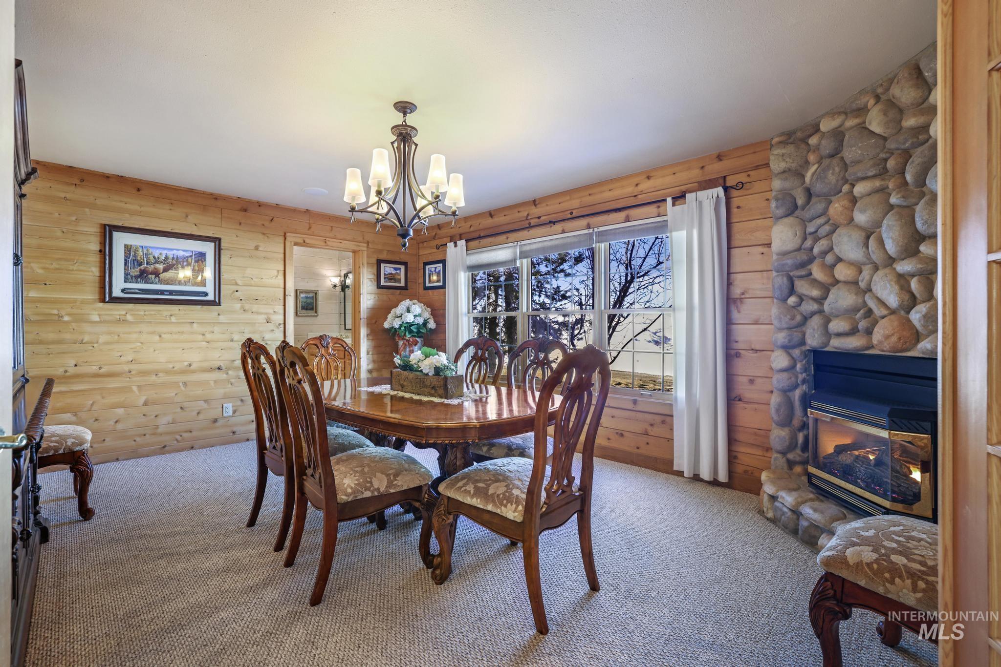 203 North Brush Road Fairfield, ID 83327 - Photo 22 of 50 Carpeted dining space featuring a chandelier, wood walls, and a stone fireplace
