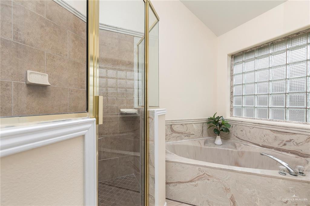 2001 Quail Lane Mission, TX 78572 - Photo 15 of 28 Spacious bathroom featuring an oversized soaking tub with stone surround, a separate shower enclosure with a brass-finish frame and tiled walls, and a glass block window providing natural light