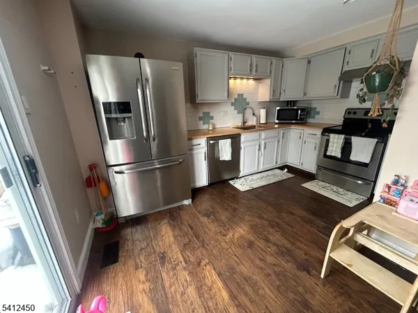 a kitchen with granite countertop a refrigerator a sink dishwasher a stove and white cabinets with wooden floor