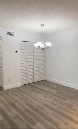 an empty room with wooden floor chandelier and windows