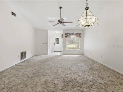 an empty room with chandelier fan and wooden floor