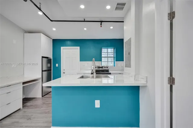 a view of a kitchen with kitchen island a sink wooden floor and refrigerator