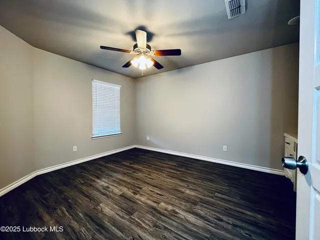 an empty room with wooden floor fan and windows