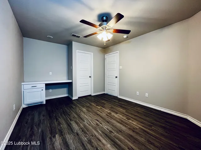 a view of an empty room with wooden floor and a ceiling fan
