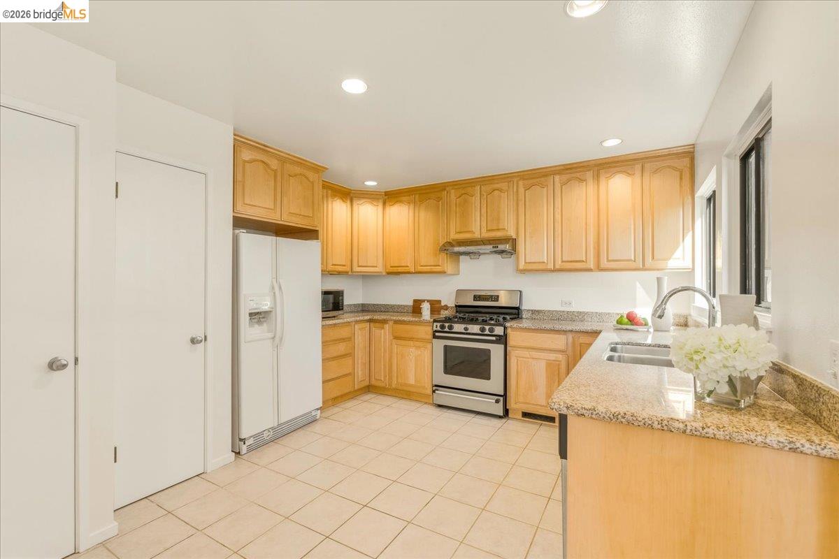1408 Henry Street Berkeley, CA 94709 - Photo 10 of 28 Kitchen with light stone countertops, stainless steel gas range oven, white refrigerator with ice dispenser, light wood finish cabinets, and recessed lighting