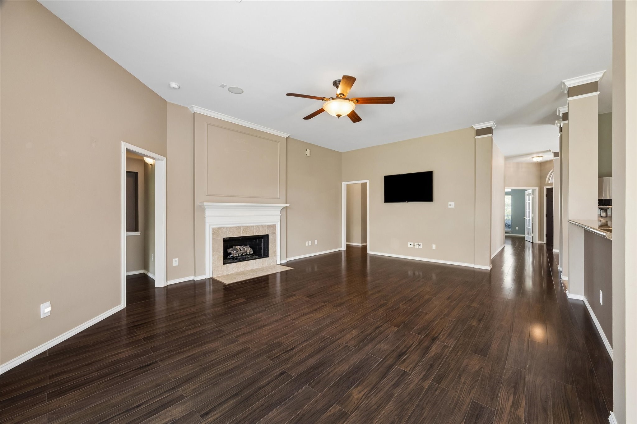 3118 Valley Court Manvel, TX 77578 - Photo 28 of 38 This spacious living room features elegant dark wood flooring, a cozy fireplace, and neutral wall colors. It includes a ceiling fan and recessed lights, with an open layout leading to adjacent rooms and a kitchen area.