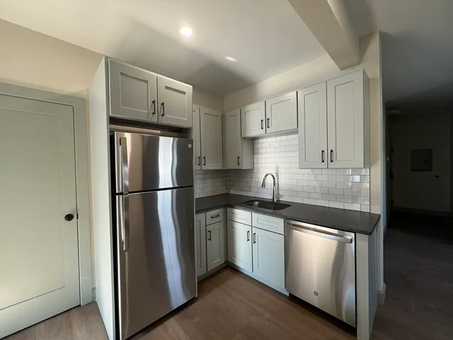 a kitchen with stainless steel appliances granite countertop a refrigerator a sink and white cabinets