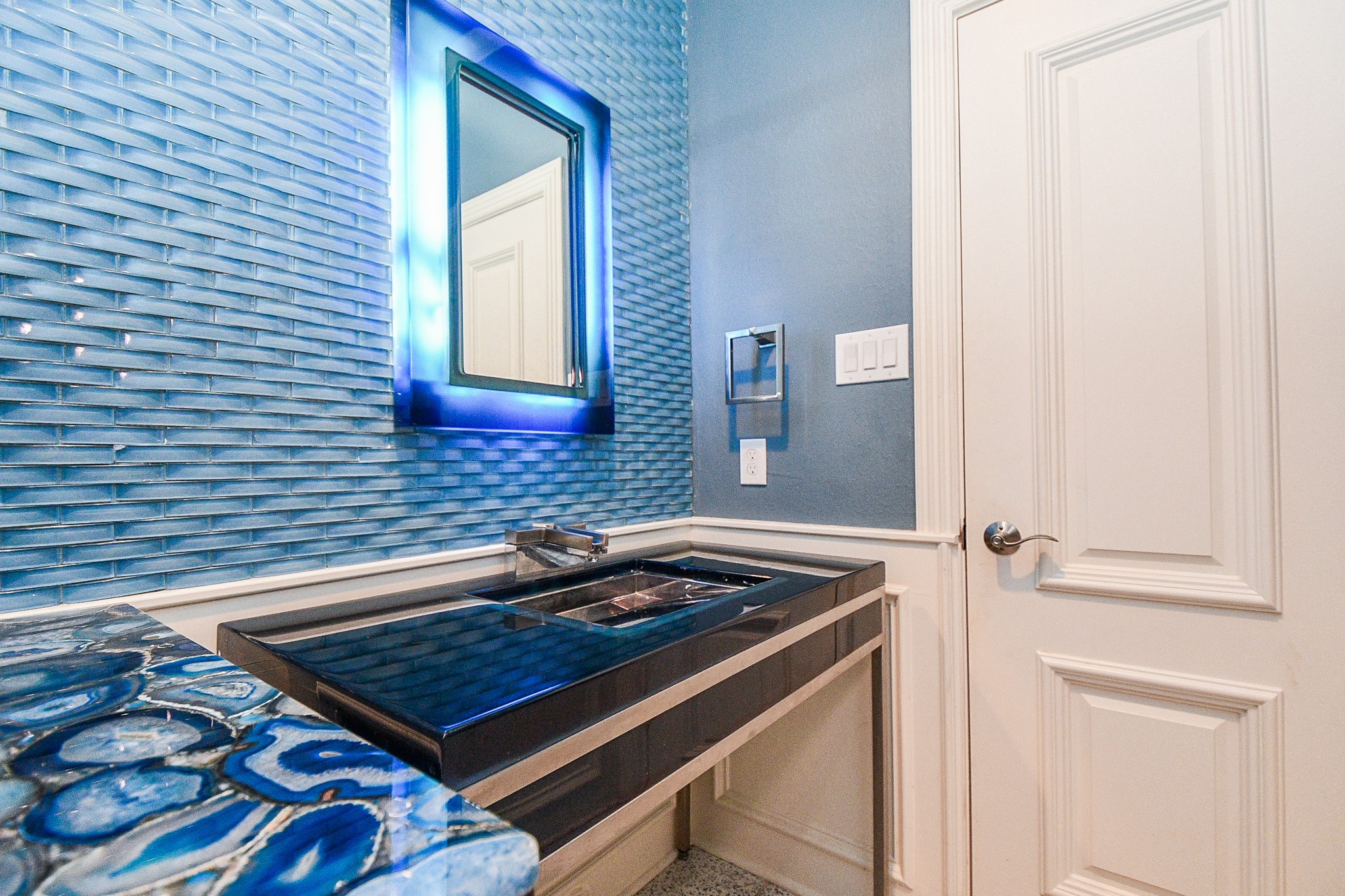 263 Wood Loop Street Houston, TX 77015 - Photo 12 of 45 This bathroom features a modern design with vibrant blue textured walls, a sleek black countertop with a stylish sink, and a striking illuminated mirror, creating a contemporary and inviting atmosphere.