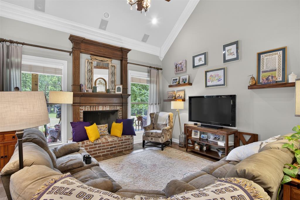 11868 Timber Ridge Drive Keithville, LA 71047 - Photo 7 of 37 Vaulted living room featuring a traditional wood-mantle fireplace with brick surround, built-in brick hearth seating, multiple windows providing natural light, and a chandelier with ceiling speakers