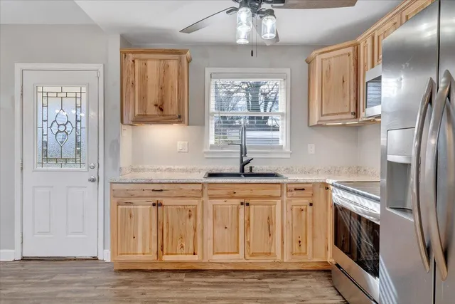 a kitchen with stainless steel appliances granite countertop a refrigerator a sink dishwasher a stove and white countertops with wooden floor