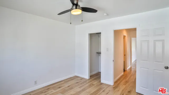 a view of an empty room with wooden floor and a ceiling fan