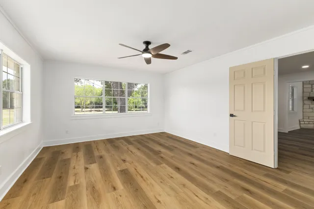 an empty room with wooden floor a ceiling fan and windows