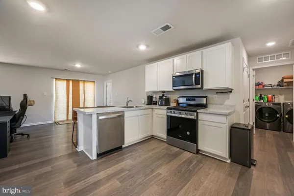 a kitchen with a microwave a stove a sink dishwasher a refrigerator and white cabinets with wooden floor