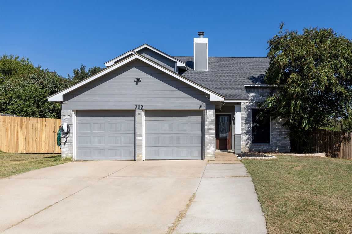 View of front of home with a chimney, concrete driveway, an attached garage, brick siding, and roof with shingles