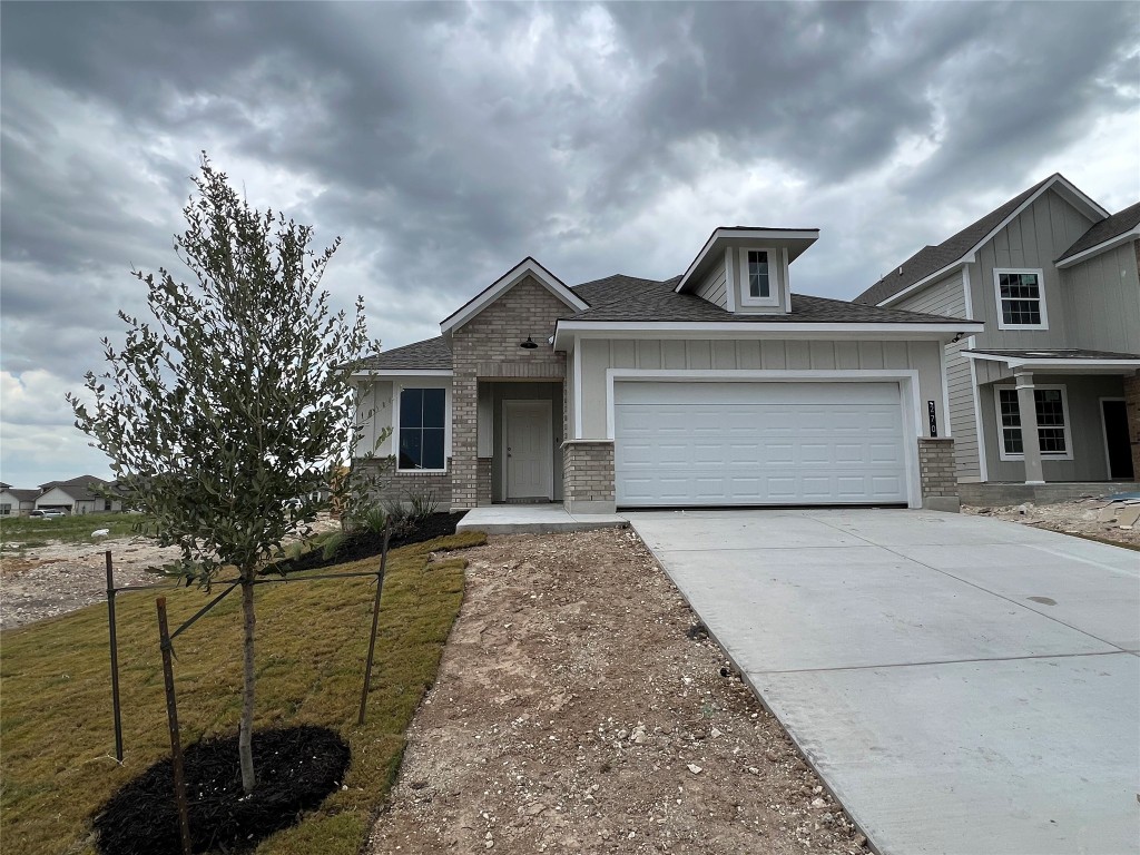Craftsman inspired home featuring driveway, a shingled roof, a front yard, a garage, and brick siding
