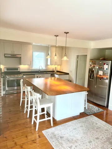 a view of a kitchen with kitchen island a sink wooden floor and stainless steel appliances