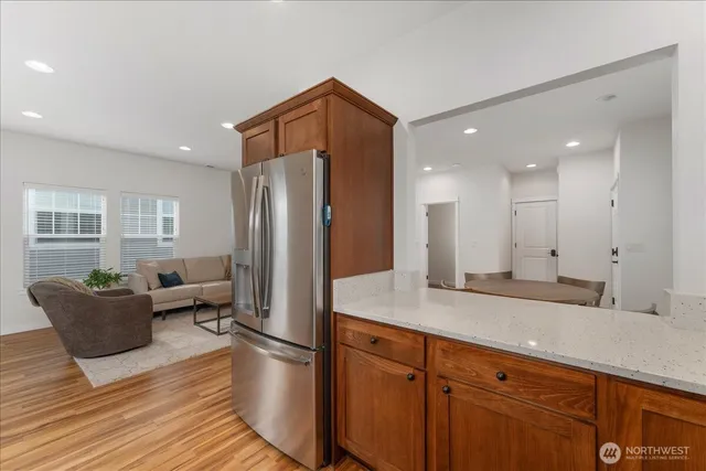 a kitchen with stainless steel appliances granite countertop a refrigerator a sink dishwasher and a dining table with wooden floor