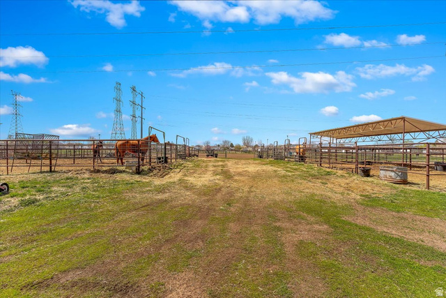 5321 South 3100th Street West Roy, UT 84067 - Photo 16 of 64 Expansive outdoor property featuring fenced enclosures, an open-air covered structure, a clear pathway, and visible power lines in the distance