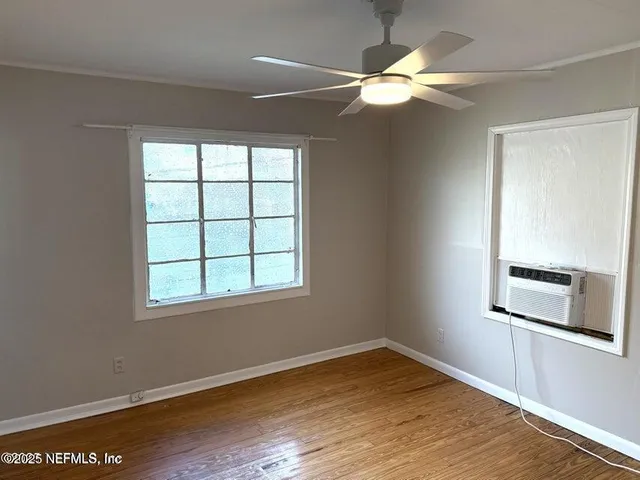 an empty room with wooden floor chandelier fan and windows