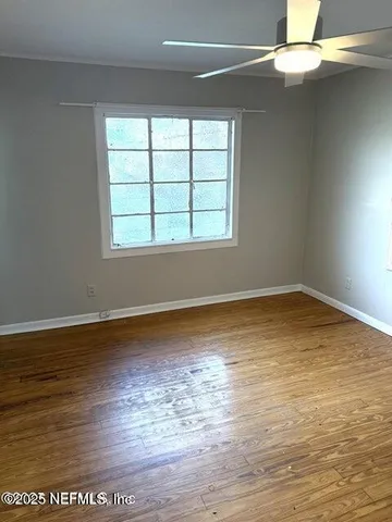 a view of an empty room with wooden floor and a window
