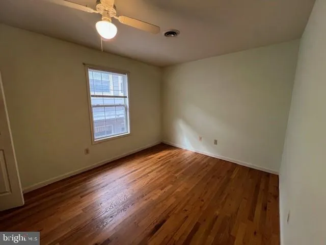 an empty room with wooden floor chandelier fan and windows