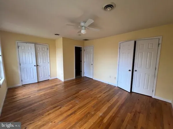 a view of an empty room with wooden floor and a ceiling fan