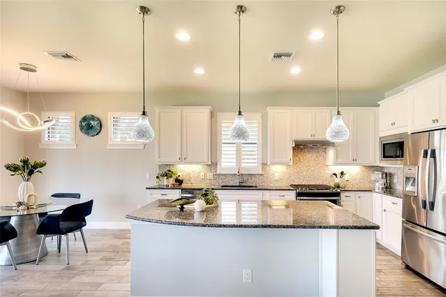 a kitchen with stainless steel appliances kitchen island granite countertop a sink a stove and a wooden floors