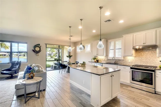 a kitchen with a stove a counter top space a sink and living room view
