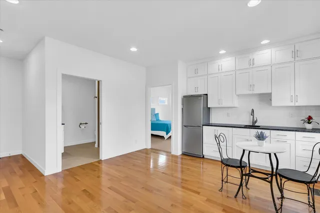 a kitchen with stainless steel appliances granite countertop a refrigerator a stove a sink and white cabinets with wooden floor