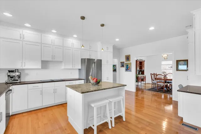 a kitchen with stainless steel appliances granite countertop a sink a stove a refrigerator and white cabinets with wooden floor