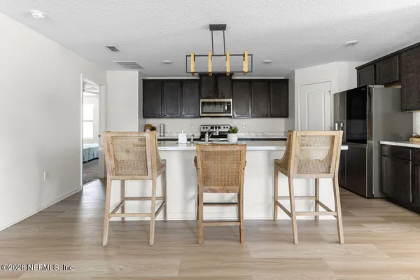 a kitchen with stainless steel appliances granite countertop a dining table chairs refrigerator and sink