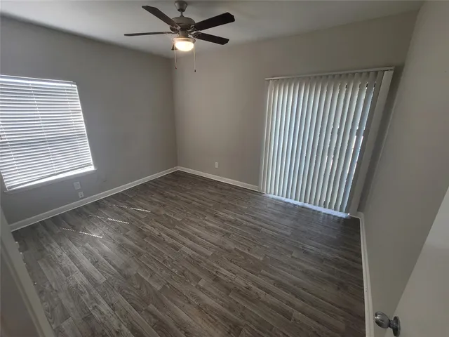 an empty room with wooden floor fan and windows
