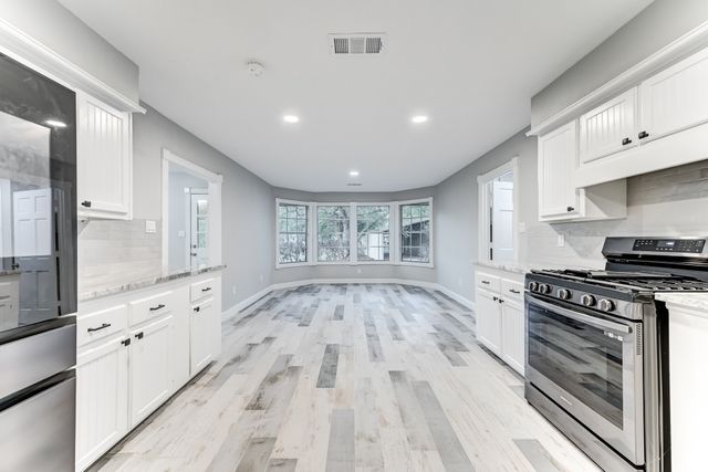 a large kitchen with granite countertop a stove top oven a sink and white cabinets