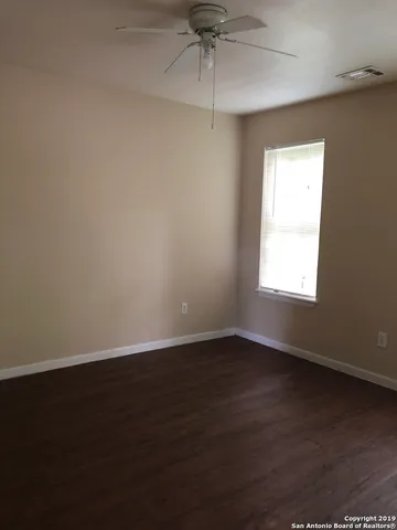 an empty room with wooden floor chandelier fan and windows