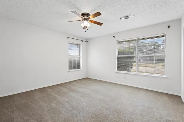 an empty room with chandelier fan and windows