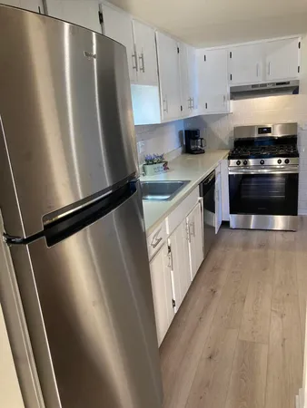 a kitchen with granite countertop a refrigerator a sink a stove and white cabinets