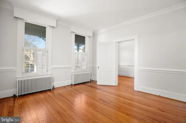 a view of empty room with wooden floor and kitchen