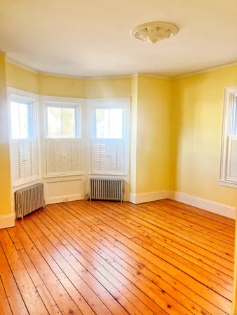 a view of an empty room with a window and wooden floor