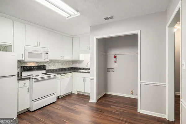 a kitchen with stainless steel appliances granite countertop a stove top oven a sink and white cabinets with wooden floor