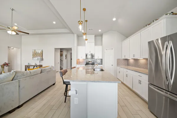 a living room with stainless steel appliances furniture a chandelier and a kitchen view