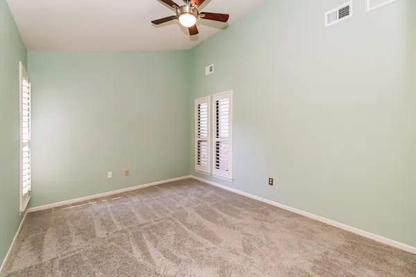 an empty room with a chandelier fan and windows