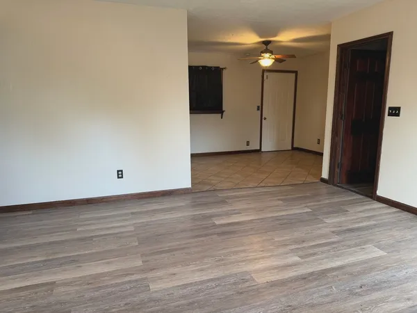 a view of an empty room with wooden floor and a ceiling fan