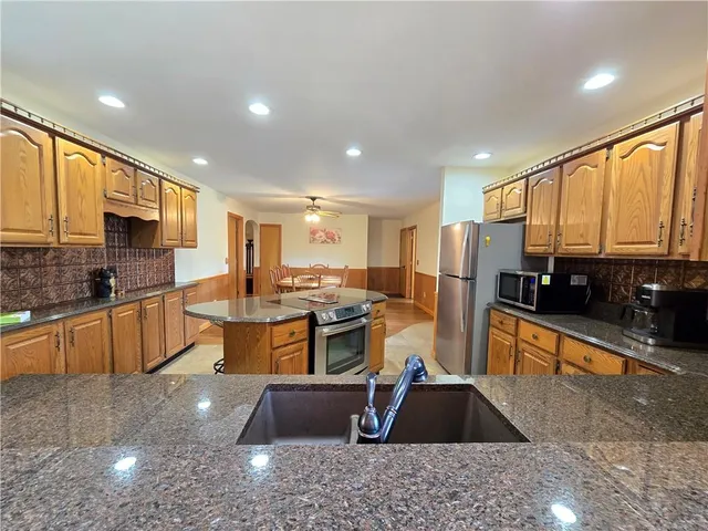 a kitchen with stainless steel appliances granite countertop a refrigerator a sink dishwasher a stove top oven a large island with wooden cabinets and floor